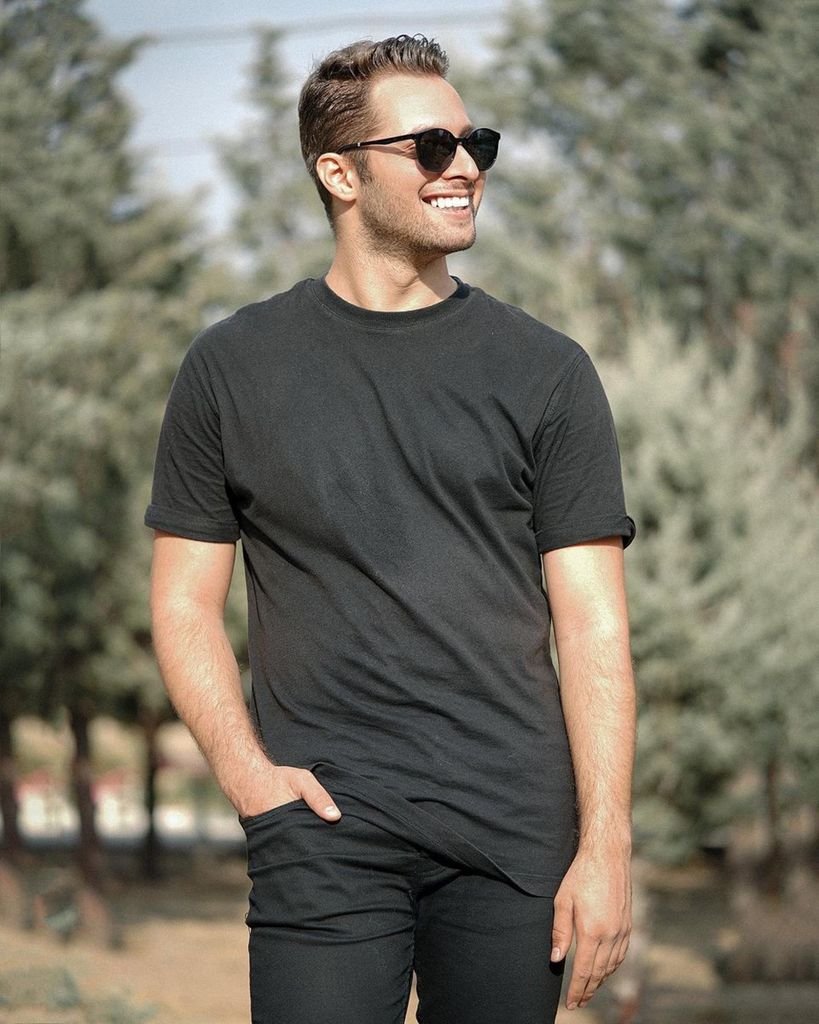 A young man with sunglasses smiling confidently in a sunny outdoor setting.